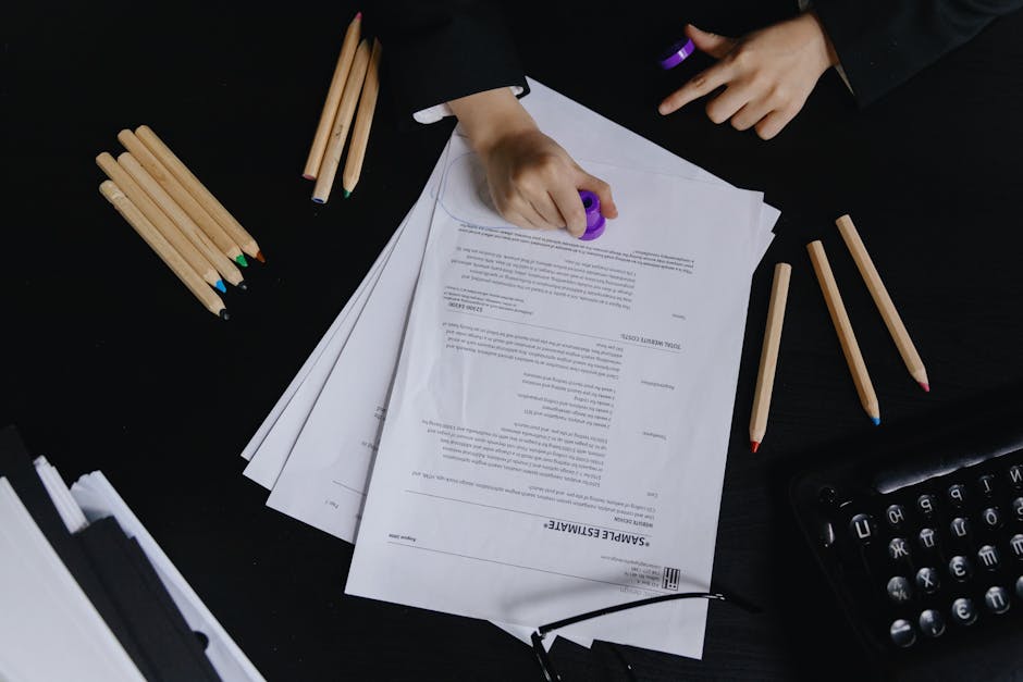 Hands working with documents and colored pencils on a black desk view.